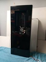 Black front panel of a water cooler standing upright, showing dispensing area and front surface with scratches and wear.