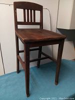 Side angle view of vintage wooden high chair on a blue cloth, showing structure and general wear on wood.
