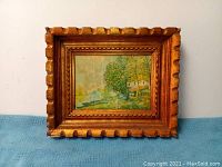 Front view of small landscape painting in a carved gilded frame showing watermarks on painting surface and wear on frame edges.