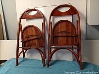 Front view of two vintage wooden folding chairs showing cut-out handles on backrests and folded seats strapped with metal hinge bars.