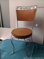 Front view of vintage metal frame chair showing wooden backrest and tan leather seat cushion with tear.