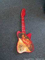 Red guitar-shaped clock with Elvis Presley image and visible clock face at bottom of guitar body.