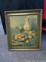 Front view of the still life painting featuring a white jug, silver bowl, various fruit on a blue cloth, framed in wood.