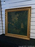 Front view of the green jungle foliage painting in an ornate gilded frame hung against slat wall.