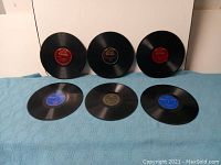 Six 78 RPM records laid out, showing a variety of colored labels including red, black, and blue Victor labels.