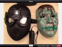 Side by side photo of two full-face masks on a table - black spider emblem mask and green glow-in-the-dark mask with fake blood splatter.