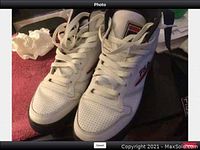 Front view of white men's Fila sneakers with laces tied showing perforated leather toe box and FILA branding on tongue and sides.