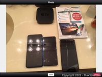 Top view of Apple iPhone 7, two Umidigi phones with cracked screens, Apple TV device, and Liquipel screen protector box.