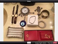 Full lot arranged on table - two watches, various jewelry pieces including bracelets, cuff, hamsa hand jewelry, red leather Cavalier wallets in box, metal dish, and wall clock with rhinestones.