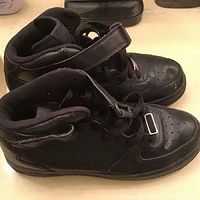 Side view of the black Nike Air Force 1 Mid sneakers showing both shoes, laces, and Velcro straps.
