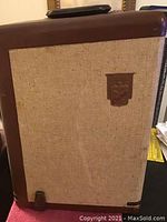 Photo of the projector showing the full front and side with beige woven fabric and brown vinyl top and edges.