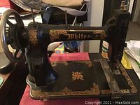 Full side view of black White vintage sewing machine with decorative gold details and hand crank wheel visible