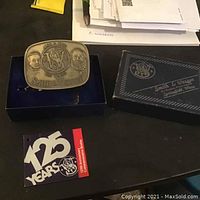 Metal Smith & Wesson commemorative belt buckle alongside original box and booklet on a dark surface.