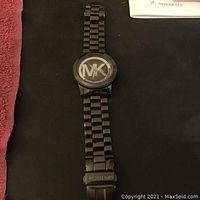 Front full view of men's Michael Kors wristwatch with black metal band and MK logo on face.