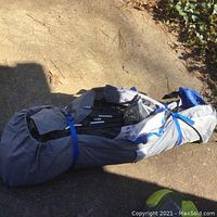 Folded camping tent in gray storage bag with blue straps on concrete floor.