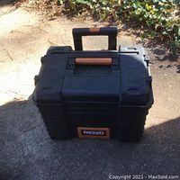 Front and top view of Ridgid black plastic toolbox with telescoping carry handle in upright position.