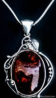 Close-up of pendant showing oval amber stone set in ornate sterling silver with swirl and leaf design.