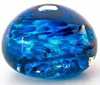 Side view of blue swirled glass paperweight showing internal patterns and surface shine
