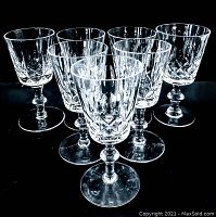 Photo shows seven vintage clear crystal wine glasses arranged closely on a black background, highlighting the faceted cut-glass pattern and decorative stems.