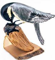 Side view of the carved wood chickadee bird figurine perched on a carved and textured wood base, stained and painted with realistic bird colors.