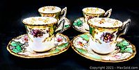 Four Coalport demitasse teacups and saucers arranged on black background showing overall design and set quantity of four cups and four saucers