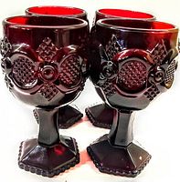 Front view showing four ruby red Avon Cape Cod wine glasses with textured raised design on bowl and hexagonal footed base.
