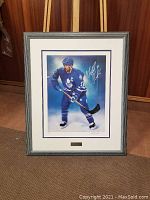 Framed full view of signed Wendel Clark print propped against wall, showing the artwork and frame.