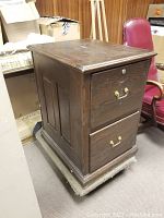 Full view of the dark wooden 2-drawer file cabinet on dolly with brass handles.