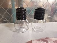 Two clear glass Libby Hottles personal tea servers with black threaded lids side by side.