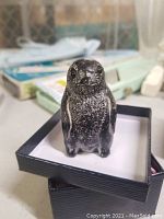 Front view of hand carved WF a Wolf penguin figurine on white platform inside a black textured box.