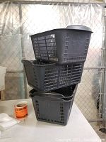 Stack of three black vintage plastic shopping baskets with ventilation holes and integrated handles.