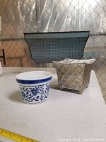Three plant pots arranged on a table: a long metal planter, a metal footed planter with floral pattern, and a blue and white ceramic planter pot.