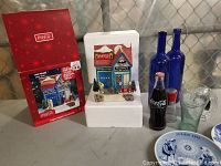 Coca Cola holiday collector lot with filling station set, branded glass items, blue bottles, and Norway plates on table