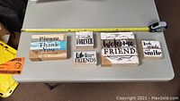 Four wooden rustic home decor signs arranged on table with measuring tape showing size.