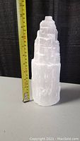 Side view of the translucent white selenite crystal tower with stepped texture and matte finish, showing its 10 inch height alongside a measuring tape.