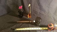 Vintage Avon glass bottle lot, showing golf clubs bottle with pink clubs and tees, giraffe bottle, and judges gavel with measuring tape for scale