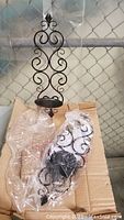 Two new black wrought-style metal wall sconces with curled scroll design, wrapped in plastic and placed on cardboard.