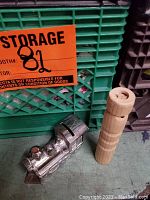 Photo showing the hand carved wooden train whistle and heavy metal train-shaped coin bank placed next to a green crate.