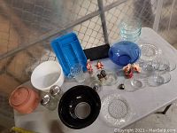 Full view of all items on table including Pyrex bowls, Marinex bowls, vintage crystal plates, FireKing pitcher, small glass containers, ceramic animal wine corks, sugar holders, and other kitchen items.