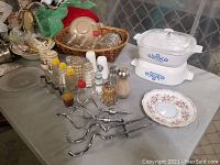 Photo showing multiple kitchenware items including salt and pepper shakers, Corningware casserole with glass lid, metal mixer attachments, Royal Albert plate, and other miscellaneous dishes