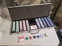 Open poker chip case showing full stacks of poker chips by color, two decks of cards, dice, and keys on the table.