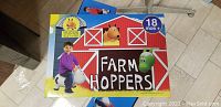 Box with cartoon barn image and toddler riding a zebra farm hopper toy, labeled 'Farm Hoppers' and indicating suitable for 18 months and older.