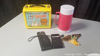 Lot showing all included items: Snoopy lunchbox, thermos bottle, calculator, and duck chalkware.