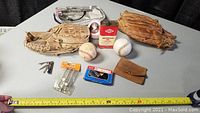 All items laid out on a table including two baseball gloves, two baseballs, oil can, string winder in box, tools in a leather case