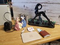 Photo showing various items including ceramic figurines, candle molds, flask and clutch on a wooden table.