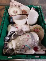 Green bin containing two white FireKing milk glass swirl bowls and multiple vintage plates and kitchen items.