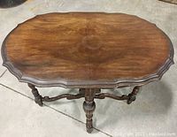 Top view of the oval scalloped wooden table top showing wear and a circular discoloration in the center.