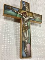 Front view of entire crucifix showing figure of Christ and colored stained glass background in wood frame.
