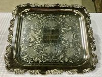 Top-down photo of ornate Sheffield reproduction square serving tray with scalloped edges on a textured white/cream surface.