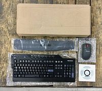 Top-down view of new Lenovo wireless keyboard, mouse, wrist rest, USB receiver, and cardboard box packaging on wooden floor